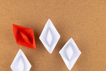 A group of white paper ship pointing in one direction and one red paper ship. Business behind an...