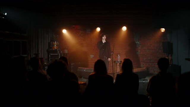 Young Caucasian male comedian performing his stand-up monologue on a stage of a small venue. Shot with ARRI Alexa Mini LF with 2x anamorphic lens