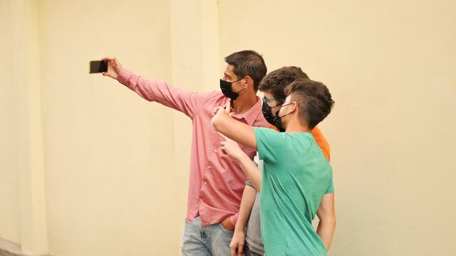 Happy friends taking a selfie and wearing protective face black masks. In the background a yellow wall. Concept of health care and the new normality