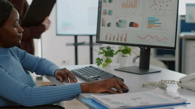 Close up of black paralyzed disabled handicapped woman entrepreneur typing on computer showing data prosessing on desktop checking graphs, financial documents, reading raports in business office