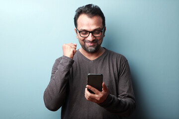 Middle aged man of Indian origin looking at his mobile phone with an excitement