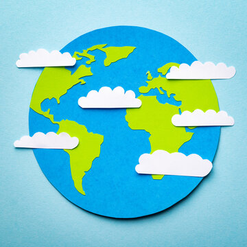 Paper cut concept of planet Earth on the blue background with paper clouds above.