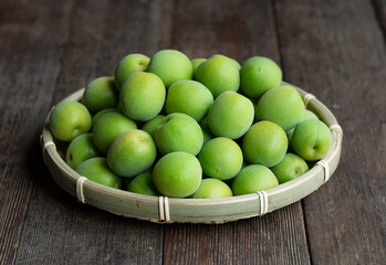 Plum fruit in a bamboo colander placed in the wooden background.