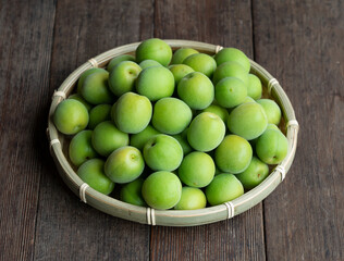 Plum fruit in a bamboo colander placed in the wooden background.