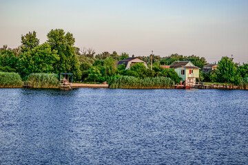 Fototapeta premium View of the holiday village on the banks of the Konka River in Kherson (Ukraine). View from the water to the coastline with private houses and piers among the reeds