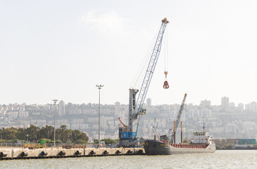 Fototapeta na wymiar A small cargo crane unloads a cargo ship at the dock at the Haifa cargo port on the Mediterranean in Israel