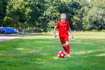 A boy in a red uniform hits a ball, does exercises, trains on the football field. Children's...