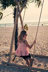 Young attractive woman is resting on seesaw on the beach at sunset.