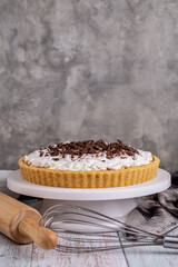 Homemade Banoffee pie with caramel, banana and chocolate topping on white cake stand.