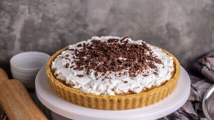 Homemade Banoffee pie with caramel, banana and chocolate topping on white cake stand. Top view flat lay background.