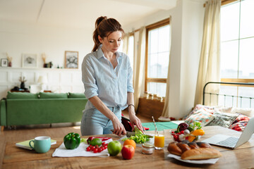 A young woman reads a recipe online on her laptop. Cooking lunch with fresh vegetables.