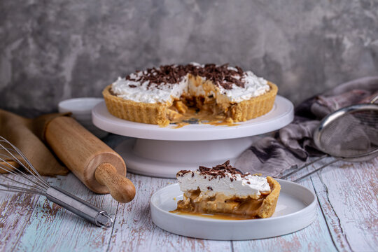 Banoffee pie with bananas, whipped cream, chocolate topping on white plate.