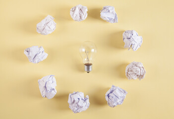 Creativity inspiration. Light bulb and crumpled paper balls on yellow background.