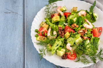 Salad with avocado, tomato and shrimps in bowl on wood table.