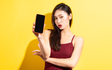 Naklejka premium Beautiful asian woman in red swimsuit and using phone on yellow background