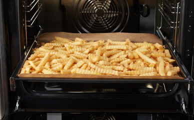Tray with many crinkle fries in open oven