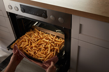 Crop person taking crinkle fries from oven