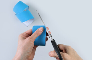 Woman trims the edges and rounded off of kinesiology blue tape to continue time of using tape.