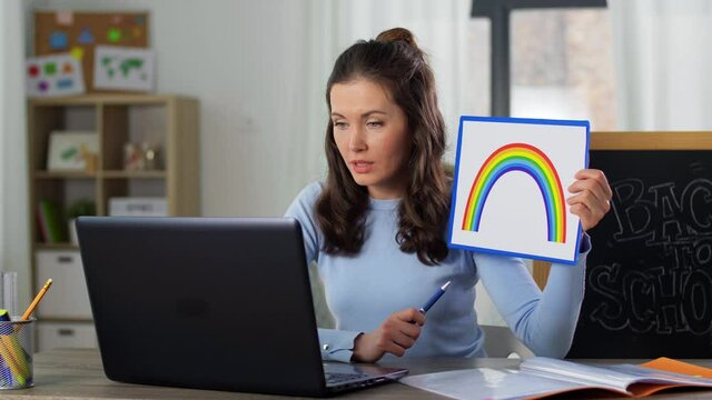distant education, primary school and teaching concept - female teacher with laptop computer and picture of rainbow having online class at home