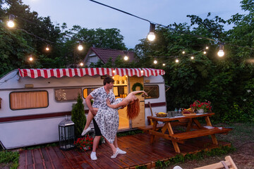 Middle-aged couple are dancing in love at the motor house in the evening. The lovers are passionately spending the weekend on budget trip in their Truck trailer. The girl's red hair flies in the wind