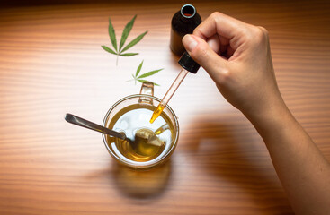 Top view of a person pouring CBD tincture made with marijuana in a hot drink.