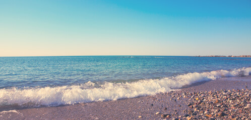 Summer panoramic view of the sea and sun on gravel beach.