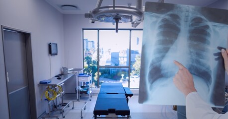 Mid section of doctor examining x-ray report against operation theatre in background