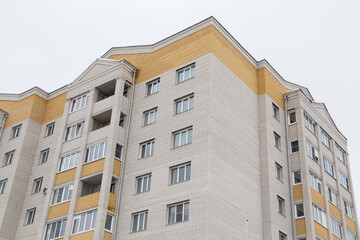 Fototapeta premium Residential high-rise building with yellow balconies and edging. Against the background of the gray sky. Modern new buildings, building facades. Real estate and urban architecture concept.