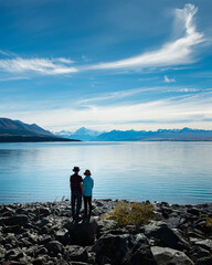 Couple standing on the shore of Lake Pukaki, enjoying the views of Mt Cook and Southern Alps, South Island. Vertical format.