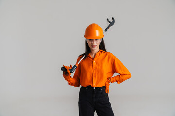 Young woman in safety glasses and helmet posing with building tool