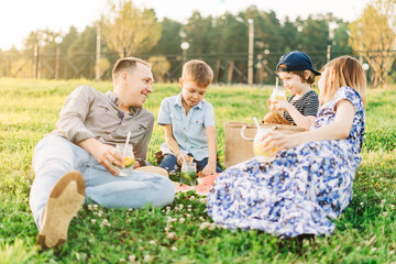 Family with two brothers, mother and father summer picnic in nature. Little children with parents hold glasses with cold lemonade in their hands. Kids boys drinking a refreshing drink from the straw. 