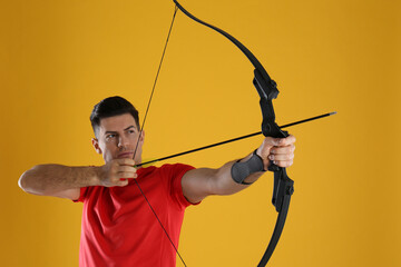 Man with bow and arrow practicing archery on yellow background