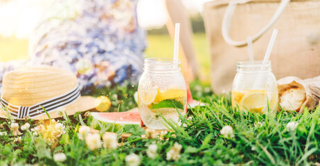 Fresh Homemade Lemonade With lime and lemon On The Grass in sunny park. Blurred green grass and people summer background. Outdoors Picnic, relaxation concept. Hello weekend.