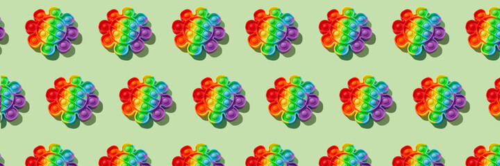 Banner pattern made with rainbow pop it fidget toy on green background. Push bubble fidget sensory toy - washable and reusable stress relief toy. Antistress toy for children or adult