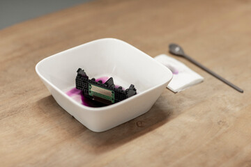 A clogged printhead from an inktjet printer being washed in a white bowl, next to a dirty paper and...