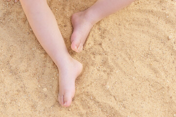 Child's feet on a background of sand. Summer background.