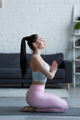 side view of young woman meditating in hero pose with praying hands and closed eyes