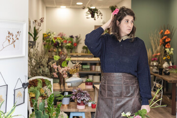 Portrait of a young woman working as florist and holding a bouquet of colourful flowers posing at the entrance of her shop, young businesswoman concept. - obrazy, fototapety, plakaty