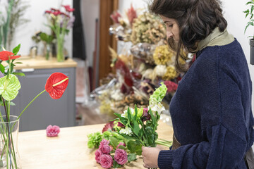 Rear view of a young woman working as florist and designing a new bouquet for wedding creation in her flower shop, young businesswoman concept.