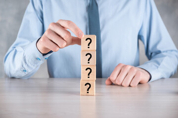 Businessman hold and put wooden cube block shape with question marks on grey table. Space for text.concept for confusion, question or solution