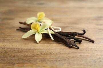Aromatic vanilla sticks and flowers on wooden table, closeup