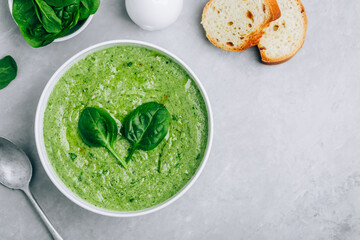 Green creamy spinach soup with baguette toasts on a gray concrete background.