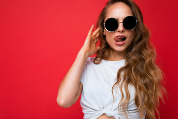 Photo shot of beautiful sexy young blonde woman wearing casual clothes and stylish sunglasses isolated over colorful background looking at camera