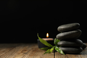 Spa stones, bamboo sprout and candle on wooden table against dark background, space for text