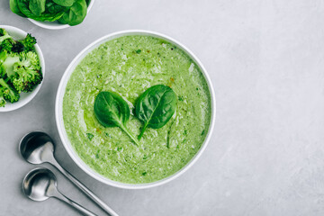 Green creamy spinach and broccoli soup on a gray concrete background.