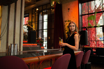 moody portraits of gorgeous blond girl with cocktail in fashion black outfit staying at the  bar in the club cafe or restaurant