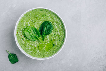 Green creamy spinach soup on a gray concrete background.