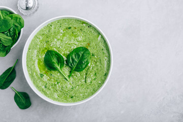 Green creamy spinach soup on a gray concrete background.