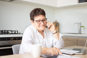 Fototapeta na wymiar Excited senior woman working at home, talking to client by phone.