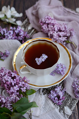 Vertical view of a cup of tea with lilac petals. Closeup.